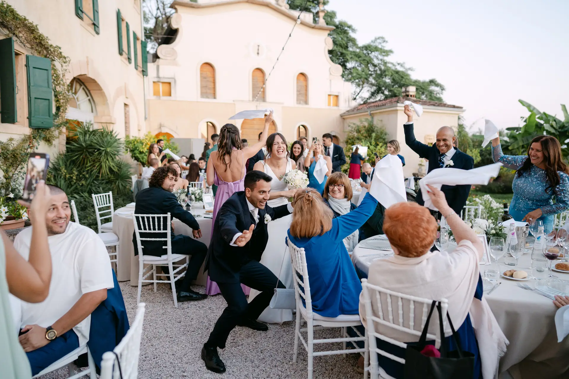Sposi accolti dagli invitati che sventolano i tovaglioli durante il ricevimento in una villa italiana